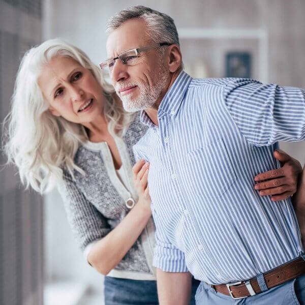 Ältere Frau stützt Partner mit Rückenschmerzen
