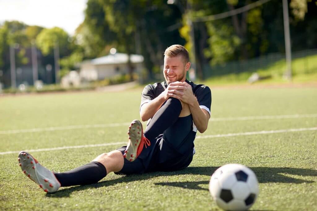 Spieler auf Fußballfeld umfasst Knie wegen Sportverletzung